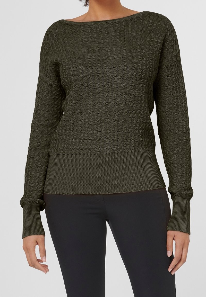 Pull en tricot vert foncé avec un motif texturé, large col bateau, et poignets et ourlet côtelés. Assorti à un pantalon noir slim.