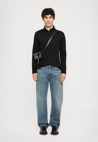 Svart langermet polo skjorte, blå løstsittende jeans, svart crossbody veske og mørke sko. Enkelt design, minimal detaljer.