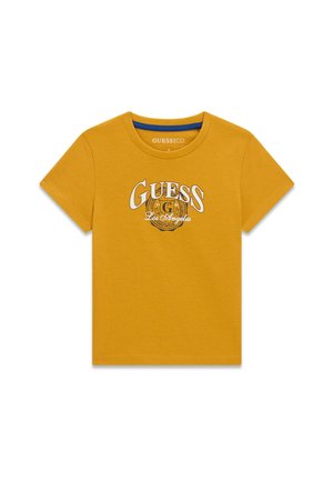 T-shirt jaune moutarde à manches courtes et à col rond, avec le logo GUESS Los Angeles sur la poitrine, sur fond blanc.