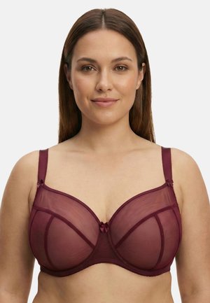 Femeie cu păr drept castaniu, purtând un sutien bordo transparent cu armătură, privirea înainte, cu o expresie neutră pe un fundal simplu.