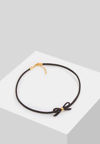 Schwarzes Wildleder-Choker mit einem kleinen Schleifendetail und goldenen Beschlägen, ausgestattet mit einer Kettenverlängerung für verstellbare Länge. Glatte Textur.