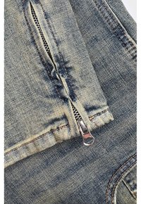 Denim stof met een vervaagde lichtblauwe kleur; heeft een zichtbare metalen rits en contrasterende stiksels, met close-up detail van de textuur van de stof.