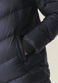 Ruka u džepu crne kviltane puffer jakne s rebrastim rukavima.