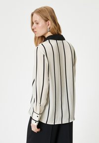 Light-colored blouse with black vertical stripes, a black collar, long sleeves, and buttoned cuffs. Smooth fabric with a flowing design.