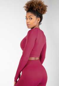 Bordeaux langemouwtop en bijpassende legging met een aansluitend ontwerp, zachte textuur en subtiele paneelaccenten. Zacht, elastisch materiaal.