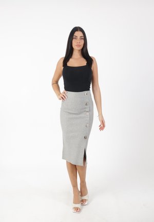 Jupe crayon grise avec fente latérale et accents de boutons en métal, associée à un débardeur noir. Texture lisse, longueur mi-mollet.