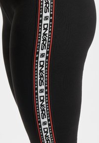 Sorte leggings med en sidestropp som har gjentatt "DNGRS" merkevare i hvitt og rødt, laget av elastisk materiale med en glatt tekstur.