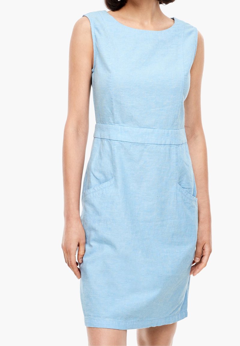 Femme portant une robe sans manches bleu clair longueur genou avec encolure ronde et poches avant, debout les bras détendus le long du corps.