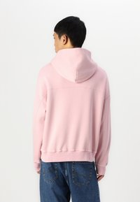 Sweat-shirt à capuche rose clair avec une coupe décontractée, présentant des détails cousus et des poignet côtelés, associé à un jean en denim bleu.