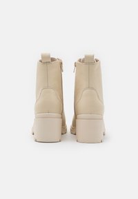 Stivaletti in pelle beige con una finitura texturizzata, punta rotonda e tacco a blocco. Presentano una cerniera laterale e un piccolo passante sul retro.
