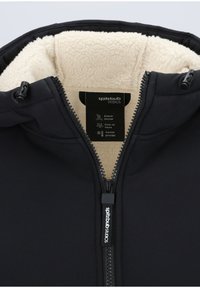Schwarze Zip-Jacke mit einem weichen, cremefarbenen Fleece-Futter. Enthält ein Etikett mit Pflegehinweisen und Markendetails.