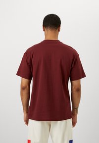Burgundy puuvillainen T-paita, jossa on klassinen pyöreä kaula-aukko, lyhyet hihat ja rento istuvuus. Minimalistinen muotoilu ilman näkyviä logoja tai kuvioita.