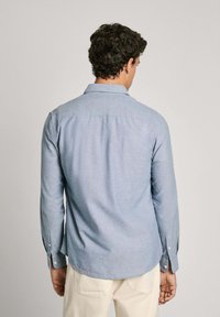 Lichtblauw button-up overhemd met lange mouwen, een kraag en een gebogen zoom; gemaakt van een gestructureerde stof. Knopen bij de manchetten en de rugnaad.