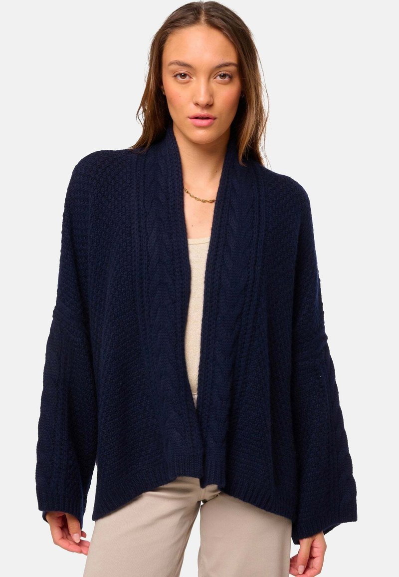 Gilet en tricot bleu marine avec une coupe décontractée, bords côtelés et motif en maille torsadée. Design à l'avant ouvert, manches oversized, texture douce.