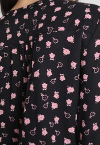 Blusa di tessuto nero con un motivo floreale in rosa e bianco, con un dettaglio plissettato sul retro e scollatura rotonda.
