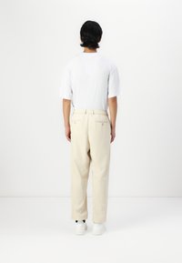 Beige trousers with a relaxed fit and elastic waistband, paired with a plain white t-shirt. Model is wearing white shoes.