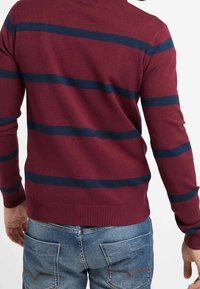 Sweter w bordowe paski z granatowymi poziomymi pasami, z prążkowanymi mankietami i dołem, noszony z niebieskimi dżinsami. Teksturowany materiał dzianinowy.