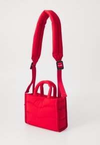 Sac à main matelassé rouge avec poignées supérieures doubles et une bandoulière réglable. La texture lisse et les détails de couture courbés rehaussent son design.
