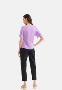 Top corto lilla a maniche corte con una vestibilità comoda, abbinato a pantaloni neri. Il top ha un scollo ampio e una consistenza liscia. I sandali presentano una suola a zeppa.