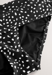 Zwart zwemkledingstof met wit spettermotief, met zichtbare binnenvoering en stikseldetails. Soepele textuur, rekbaar materiaal.