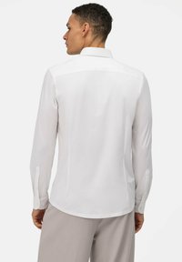 Weißes Langarmshirt mit klassischem Kragen, knöpfbaren Manschetten, glatter Textur und taillierter Passform, von hinten gezeigt.