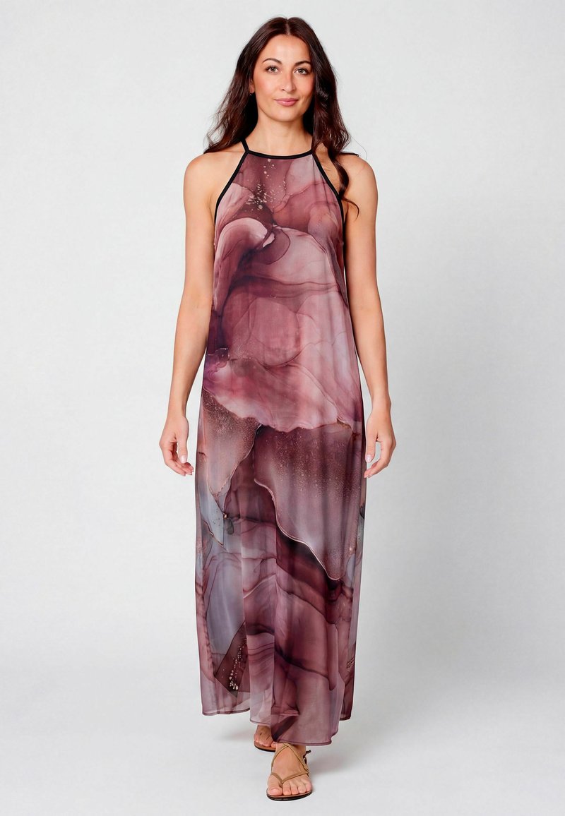 Femme portant une robe sans manches longue jusqu'au sol avec un motif marbré violet et rose, debout devant un fond clair uni.