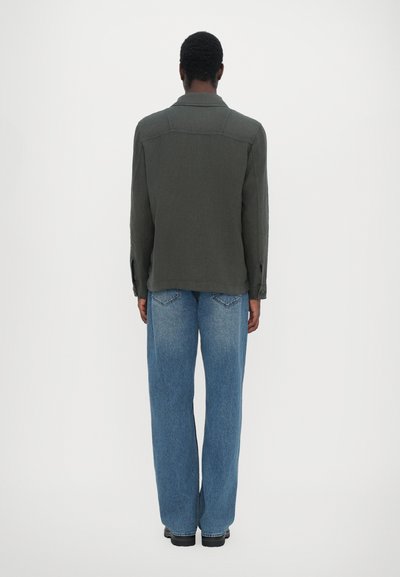Veste grise à col, avec une coupe décontractée, assortie à un jean en denim bleu clair à coupe ample, vue de dos sur fond uni.