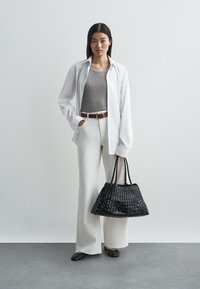 Fonott fekete kézitáska két fogóval, fehér gombos inggel, szürke trikóval, fehér bő szárú nadrággal és fekete lapos cipővel párosítva.