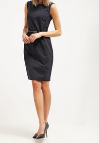 Granatowa sukienka bez rękawów o dopasowanym kroju, z paskiem w talii i gładką fakturą. Dobrana z czarnymi szpilkami.