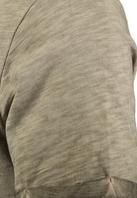 Primo piano di un tessuto beige lavorato a maglia con un motivo testurizzato sottile e cuciture visibili lungo le giunture.