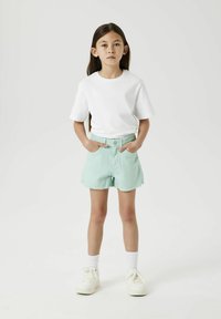 Witte T-shirt met korte mouwen gecombineerd met mintgroene spijkerbroekshorts met een rafelige zoom. Witte sneakers en crewsokken maken de outfit compleet.