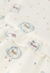 Tela blanca con estampados de animales bordados en azul, rojo y dorado, con un borde rizado. Textura suave y diseño delicado.
