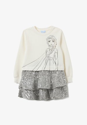 Sudadera color crema con un contorno negro de un personaje en el frente, combinada con una falda de lentejuelas plateadas en capas.