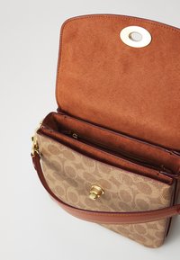 Sac à main en cuir marron avec un extérieur à motif beige. L'intérieur présente une doublure en tissu doux de couleur marron et une fermeture à pression dorée. Deux compartiments visibles.