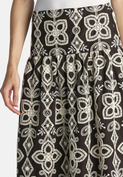 Zwarte rok met gedetailleerde witte haakwerk bloemen- en geometrische patronen, geplooid bij de taille, gedragen met een ingestopt wit topje.