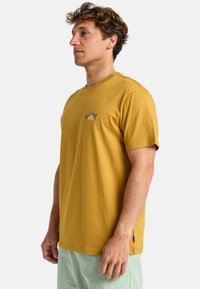 Sennepsgul bomulds-T-shirt med korte ærmer, en rund halsudskæring og et lille grafisk logo på brystet i en afslappet pasform.