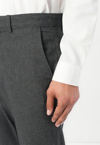 Gray textured trousers with a slim fit, featuring side pockets and a waistband, paired with a white long-sleeve shirt.