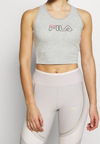 Šedý zkrácený top bez rukávů s logem "Fila", spárován s béžovými legínami s prohnutými zlatými akcenty a jemnou texturou.