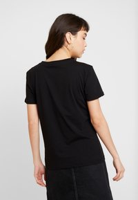 T-shirt en coton noir à manches courtes, col rond et coupe décontractée. Le dos présente une texture lisse et un design simple.
