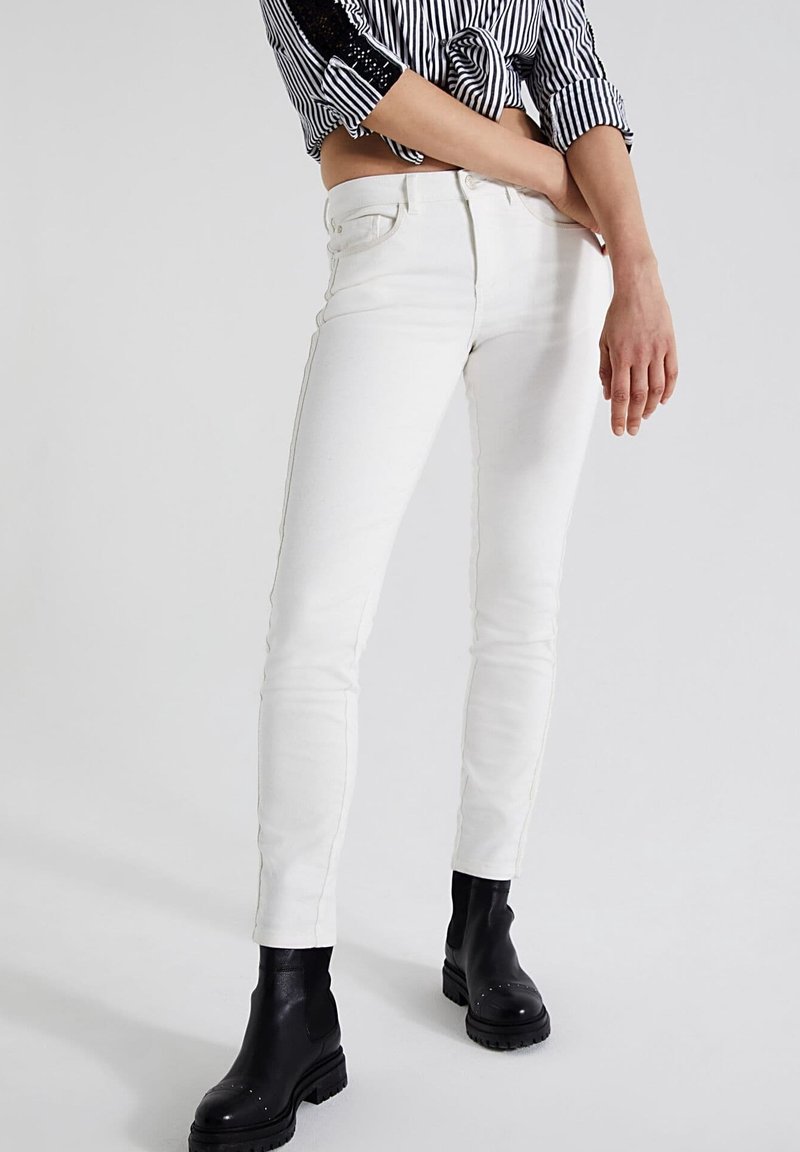 Jeans ajustados blancos hechos de una mezcla de algodón, con bolsillos delanteros, un diseño clásico de cinco bolsillos y sutiles detalles de costura.