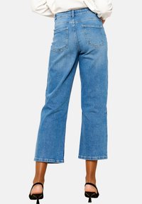 Ljust blå, högmidjade jeans med vida ben, med två bakfickor och en ren fåll, kombinerade med svarta klackar med remmar.