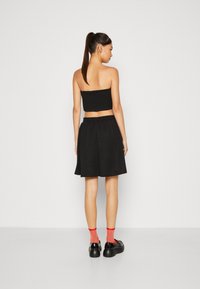 Svart strapless cropped topp paret med et svart skjørt. Glatt, lett stoff, elastisk midjebånd, og svarte sko med rød sokk som aksent.