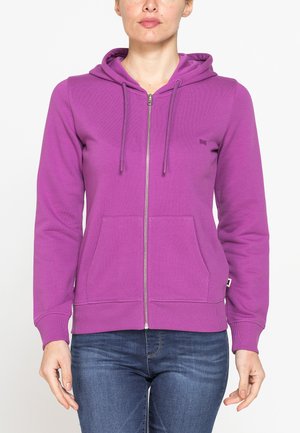 Donna che indossa una felpa con cappuccio viola con cerniera, tasche frontali e coulisse, abbinata a jeans blu, mostrata dal collo ai fianchi.