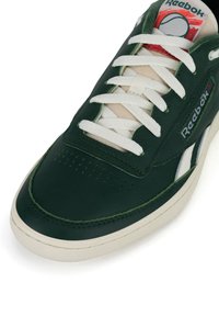 Tmavozelené tenisky Reebok s bielymi šnúrkami, bielou podrážkou a logom na boku a jazyku.