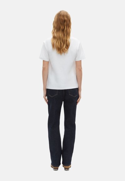Hvid bomulds T-shirt med korte ærmer, parret med mørkeblå denim jeans, der har lige ben og minimale syninger.