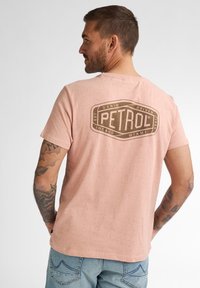 Světle růžové bavlněné tričko s tečkovanou texturou. Na zadní straně se nachází velké hnědé logo "PETROL". Krátké rukávy, kulatý výstřih.