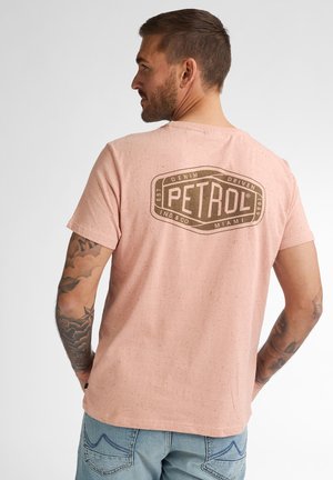 Tricou din bumbac roz deschis cu textură măruntă. Prezintă un mare logo maro "PETROL" imprimat pe spate. Mâneci scurte, guler rotund.
