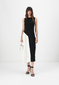 Robe noir et blanc avec un design ajusté sans manches, comportant un panneau plissé blanc d'un côté et un tissu noir lisse. Accentuée par des chaussures à talons noirs.