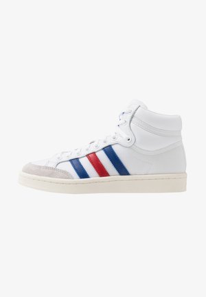 Biały wysokiej cholewce sneaker z niebieskimi i czerwonymi paskami, białą podeszwą i beżowym zamszowym noskiem, widziany z boku.