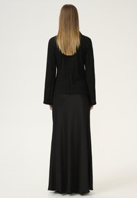 Black long-sleeve textured jacket with a fitted waist, paired with a flowing black maxi skirt, both displayed against a neutral background.